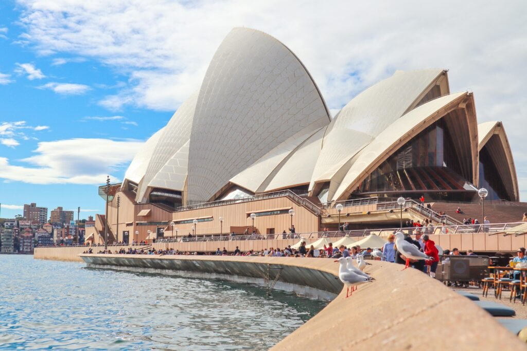 Sydney Opera House with tourists and waterfront view on a sunny day.